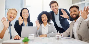 Group photo of business professionals waving while sitting at a conference table